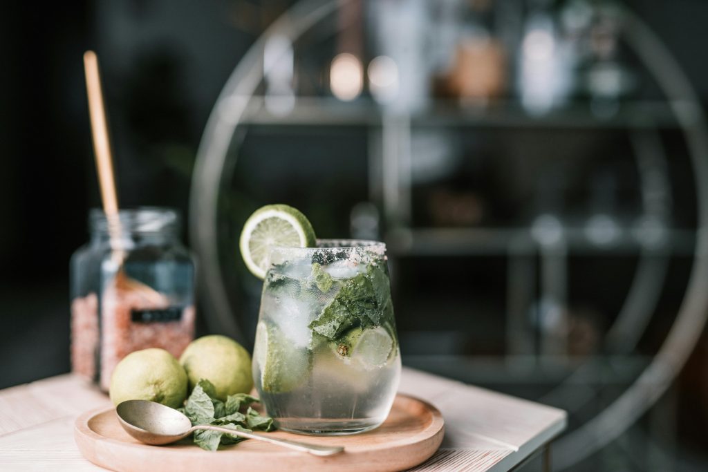 A mojito cocktail is served on a plate over a table. The srping mojiot has the classic ingredients: white rum, soda, sugar, fresh mint. Two full limes are placed next to the glass with the mojito.</p>
<p>Photo by Taryn Elliott via Pexels.com